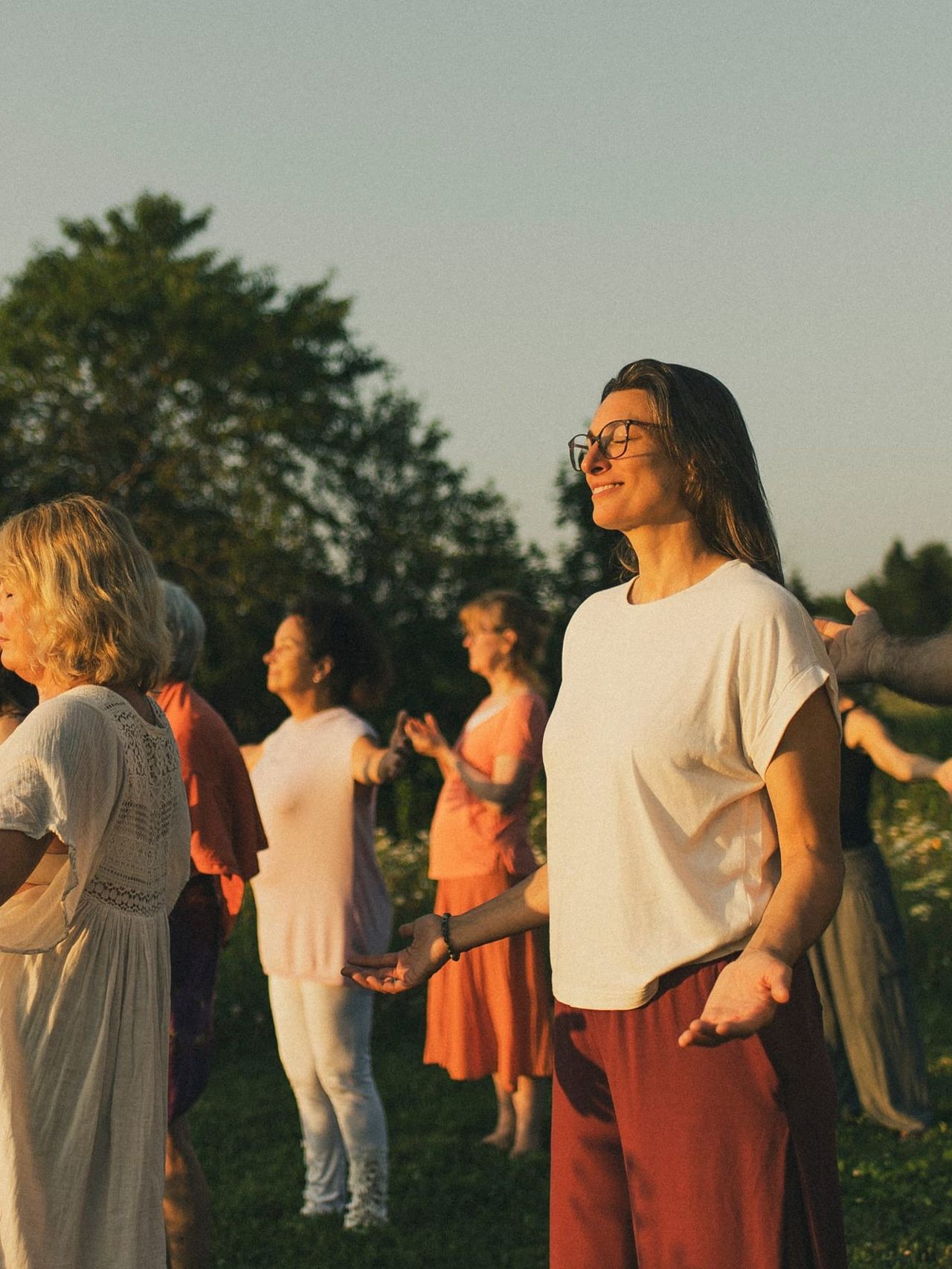 Participants de profil, yeux fermés, paumes ouvertes vers la lumière dorée du couchant.