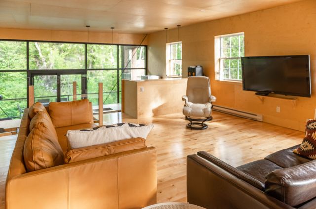Salon lumineux avec canapés en cuir et grandes baies vitrées sur la nature