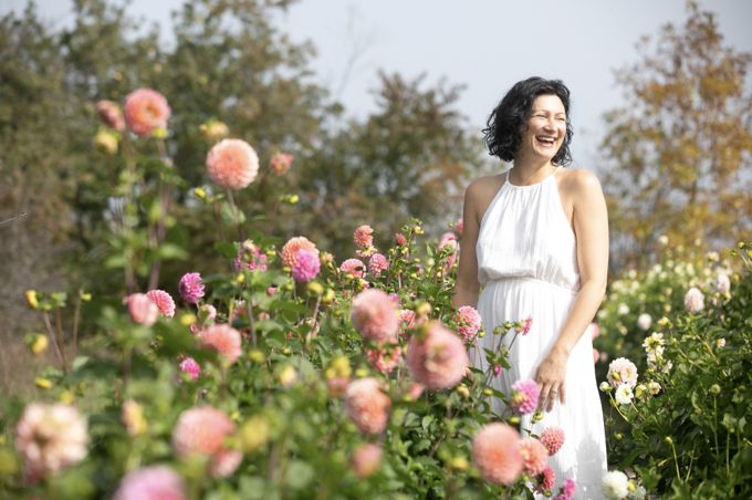 Christine Dion riante en robe blanche, au milieu d'un massif de dahlias roses.
