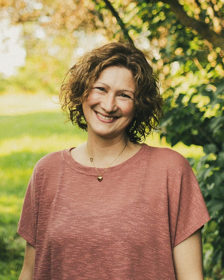 Christine Dion souriante sous une arche d'arbres, dans la lumière dorée du jardin.