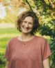Christine Dion souriante sous une arche d'arbres, dans la lumière dorée du jardin.